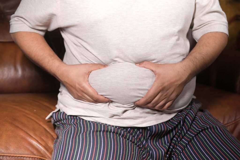 pexels photo 11911053 A close-up view of a man holding his tummy while sitting on a couch, highlighting lifestyle choices.